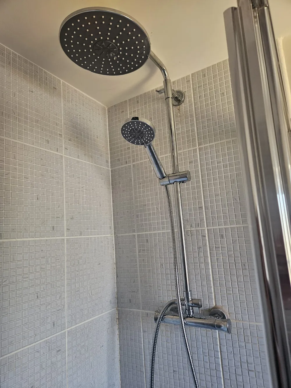 Matte black rainfall shower head and riser fitted in a grey tiled shower enclosure