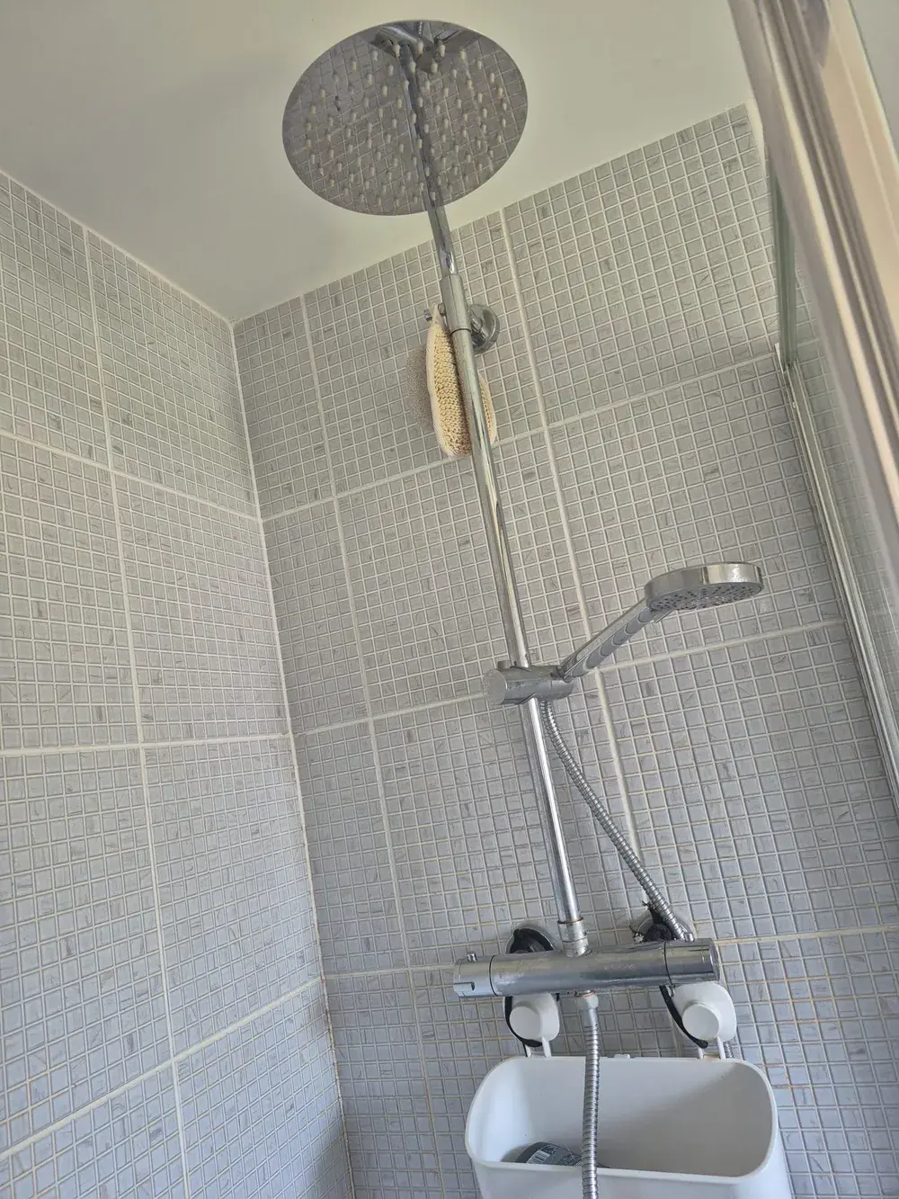 Rainfall shower head and thermostatic riser fitted in a grey mosaic tiled shower