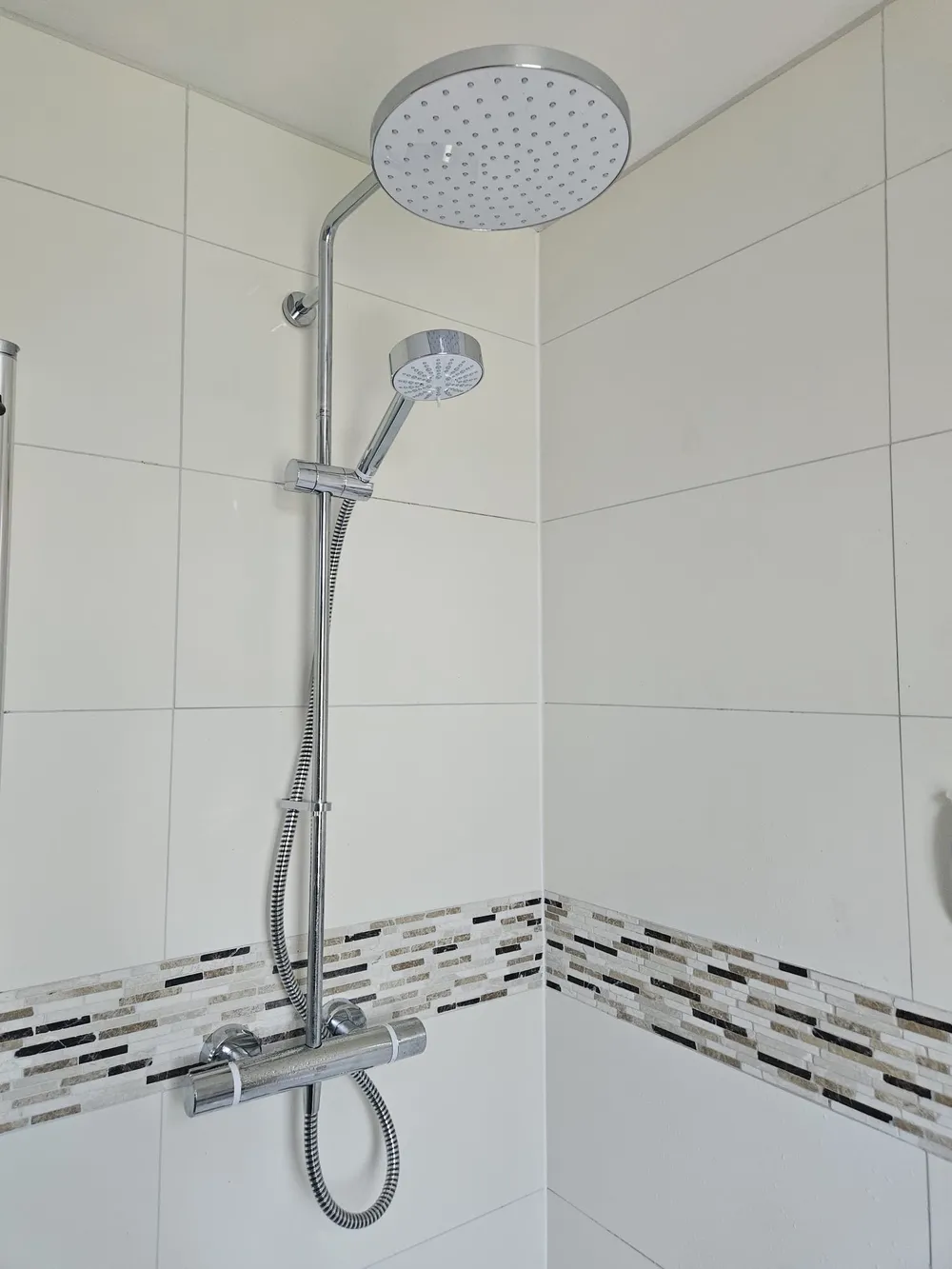 Chrome thermostatic shower with rainfall head and riser rail fitted in a white tiled Coventry bathroom
